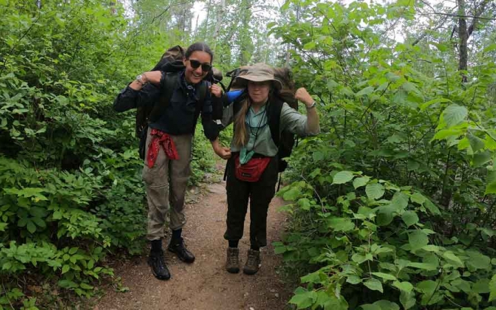 two students wear backpacks and flex their arm muscles on an outward bound course in minnesota